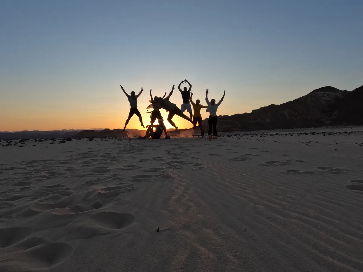 Reisegruppe springt als Silhouette vor dem Sonnenuntergang in der Wüste Sinai