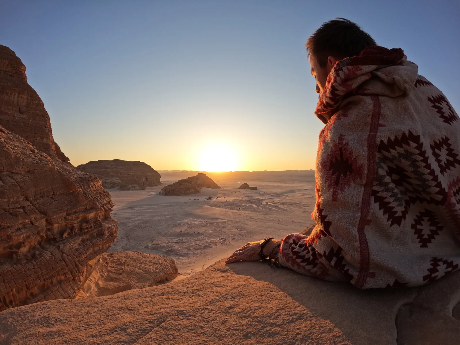 Reisender sitzt in Decke gehüllt und schaut auf den Sonnenuntergang in der Wüste Sinai