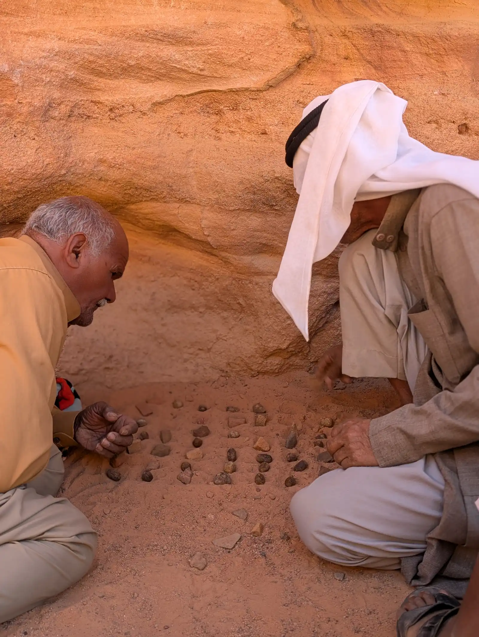 Zwei Männer spielen ein altes Steinspielbrett im Fels der Wüste Sinai