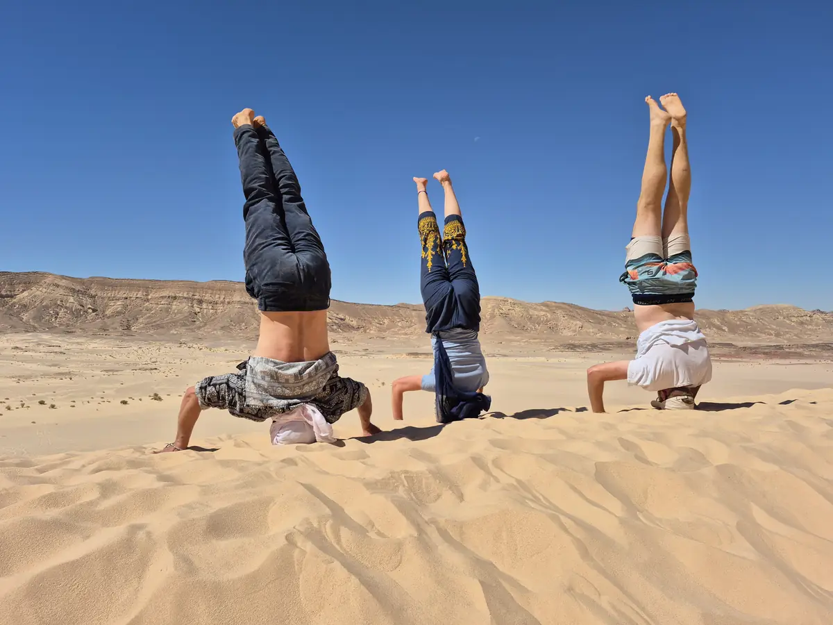 Drei Menschen üben Kopfstand auf einer Sanddüne in der Wüste des Süd-Sinai