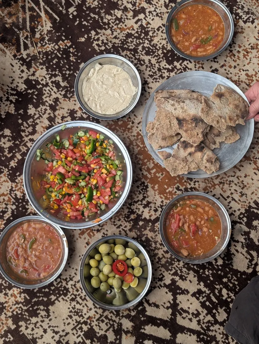 Beduinisches Essen auf einem Teppich serviert — Tomatensalat, Hummus, Oliven, Bohnen und frisches Fladenbrot in der Wüste des Süd-Sinai