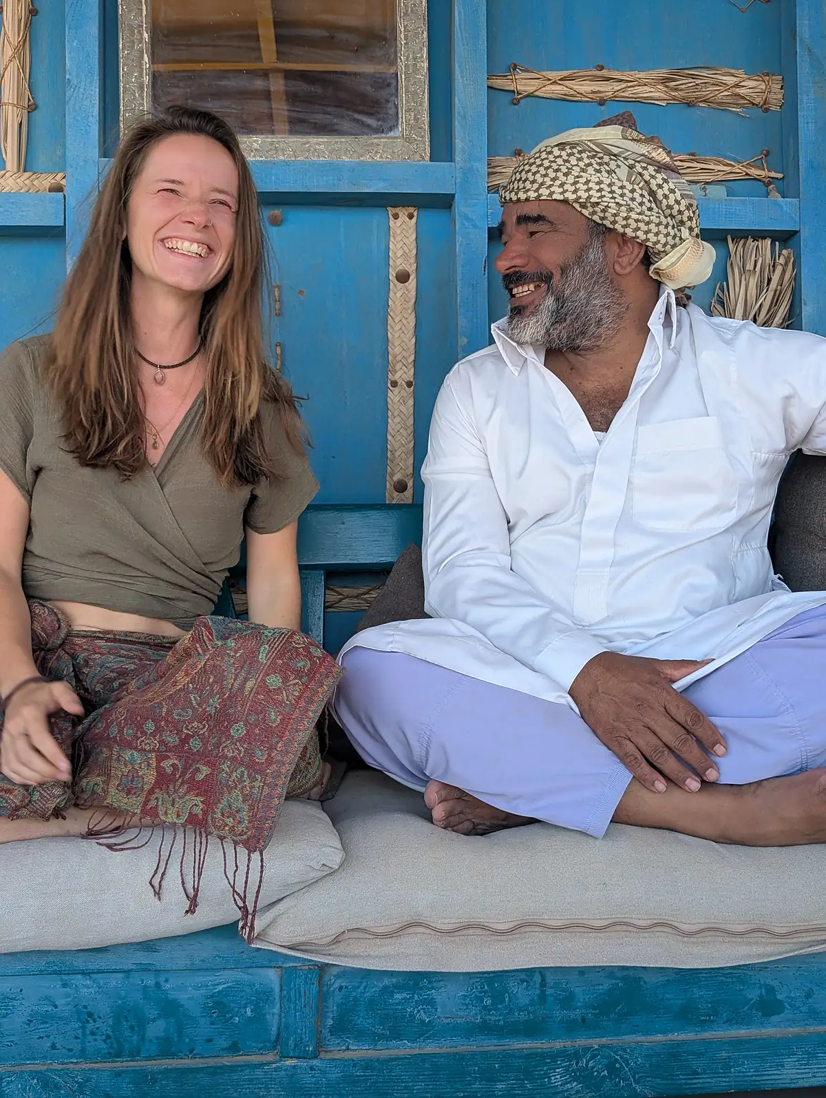 Elena und Swualim sitzen lachend vor der blauen Holzwand des RockSea Camps in Nuweiba — Süd-Sinai