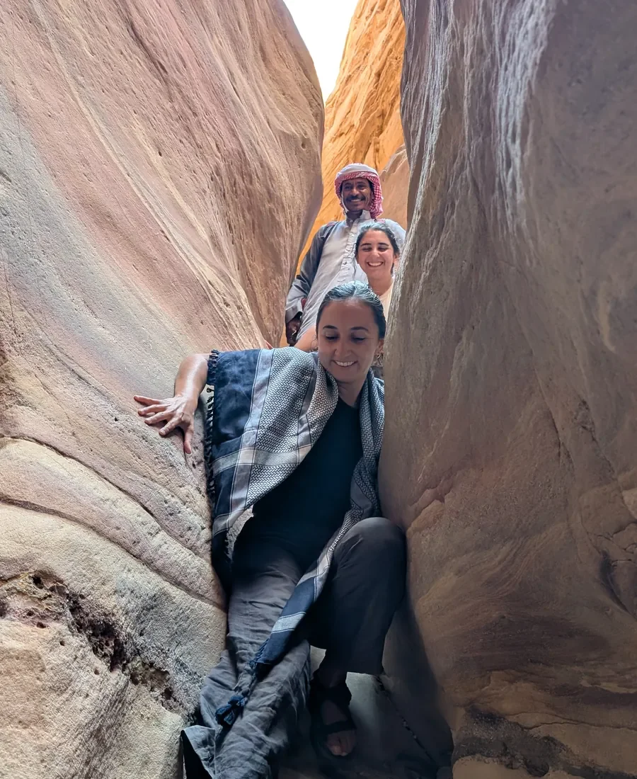 Drei Personen lachen beim Durchqueren einer engen Sandsteinpassage im Canyon des Süd-Sinai — mit Swualim, Tarabin-Beduine und Wüstenführer