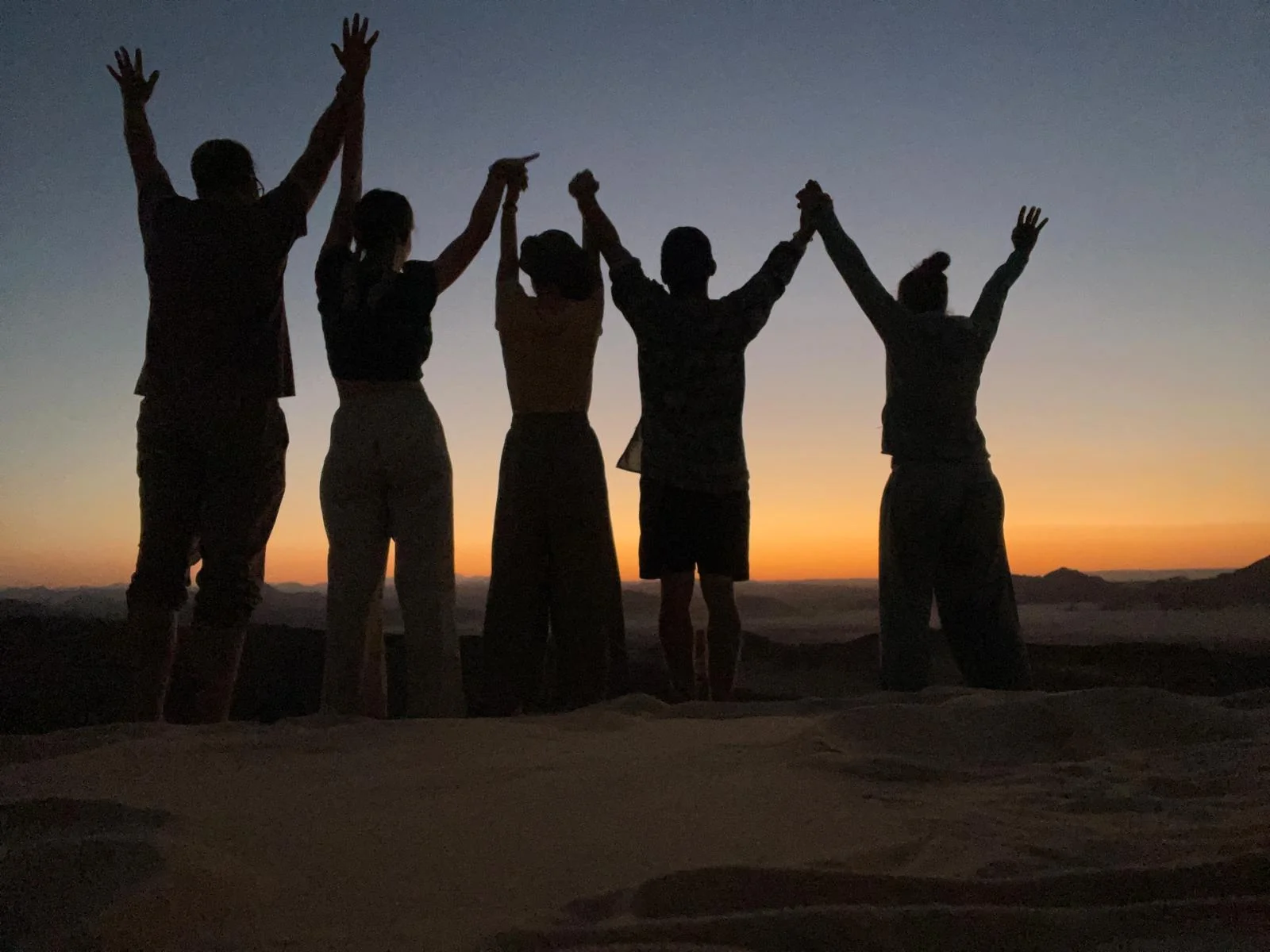 Reisegruppe streckt als Silhouette die Hände in den Himmel vor dem Sonnenuntergang in der Wüste Sinai